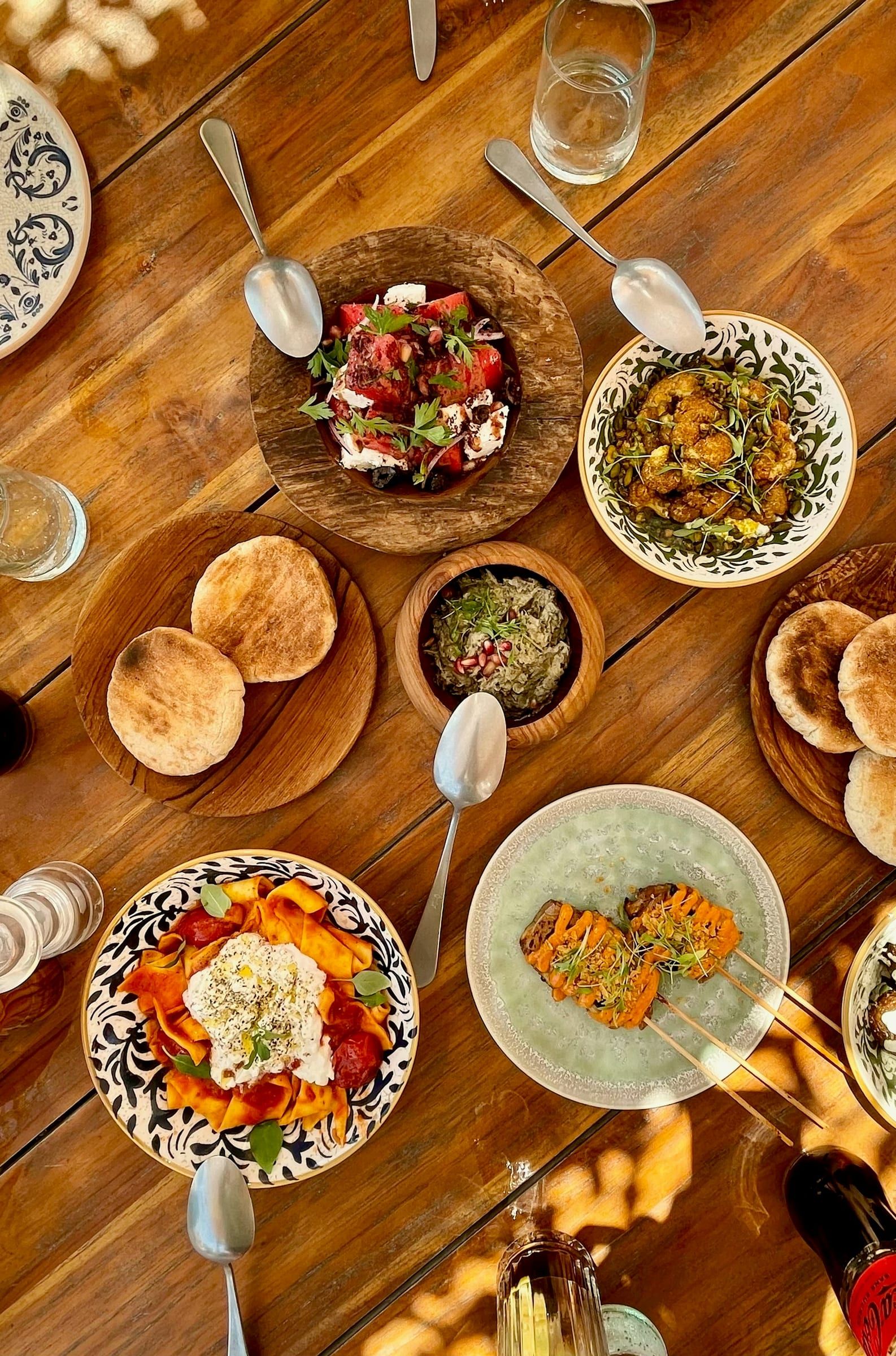 Shared dishes on a wooden table: flatbreads, dips and salads in hand-made ceramic bowls, seen from above.